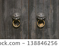 Pair of Antique Brass Lion Head Door Knockers on Weathered Wooden Double Doors 138846256