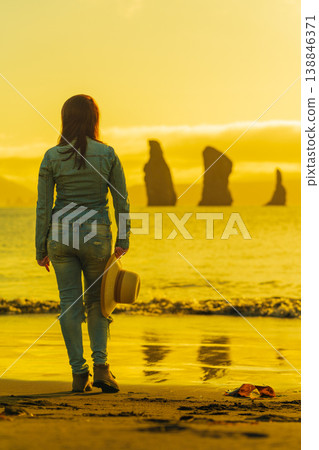 Woman from behind on sandy beach watching golden sunset over the ocean Woman from behind on sandy beach watching golden sunset over the ocean 138846371