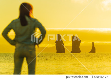 Woman watching golden sunset over silhouette rock formations in the ocean on the horizon Woman watching golden sunset over silhouette rock formations in the ocean on the horizon 138846376
