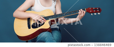 Unrecognizable woman playing acoustic guitar, closeup on hands and fretboard against blue background Unrecognizable woman playing acoustic guitar, closeup on hands and fretboard against blue background 138846469