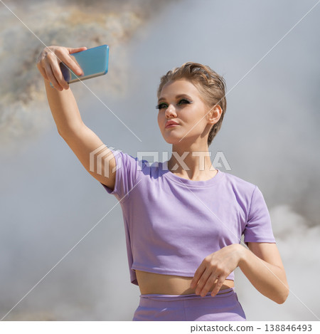 Stylish woman in purple outfit taking a selfie with a phone against a steamy, geothermal background Stylish woman in purple outfit taking a selfie with a phone against a steamy, geothermal background 138846493