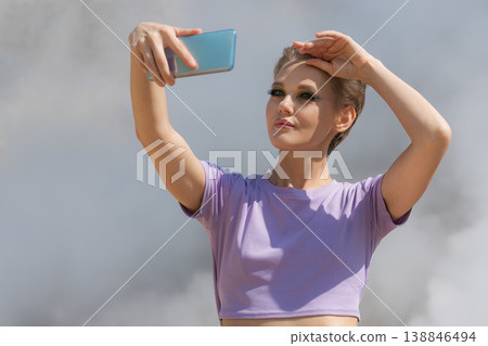 Stylish woman with short hair takes a selfie with smartphone, shielding eyes from sunlight outdoors Stylish woman with short hair takes a selfie with smartphone, shielding eyes from sunlight outdoors 138846494