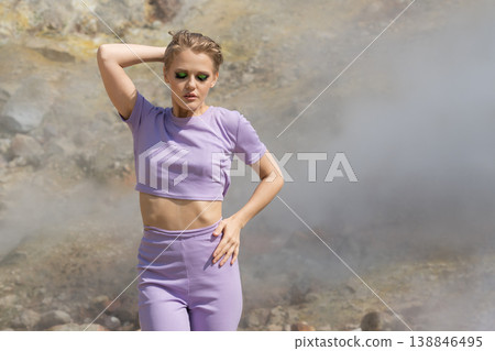 Stylish woman in lavender outfit with bold green eyeshadow posing in a surreal, steamy landscape Stylish woman in lavender outfit with bold green eyeshadow posing in a surreal, steamy landscape 138846495