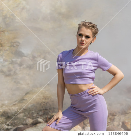 Confident woman with short hair in purple athleisure outfit posing in a steamy, rocky landscape Confident woman with short hair in purple athleisure outfit posing in a steamy, rocky landscape 138846496