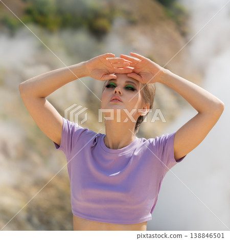 Stylish woman with dramatic green makeup in a purple top shielding her eyes from bright sun outdoors Stylish woman with dramatic green makeup in a purple top shielding her eyes from bright sun outdoors 138846501
