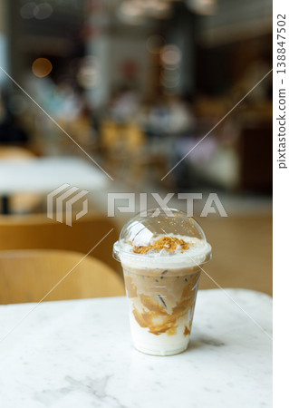 Cup of iced milk caramel latte coffee topped with biscuit on table by the window. Cup of iced milk caramel latte coffee topped with biscuit on table by the window. 138847502
