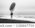 Strong woman with dramatic makeup holds surfboard on her head black sand beach 138847750