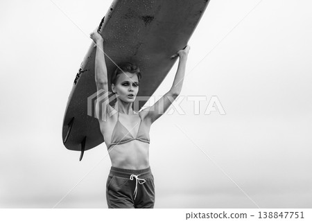 Strong woman with dramatic makeup holding surfboard over her head in black and white Strong woman with dramatic makeup holding surfboard over her head in black and white 138847751