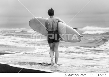 Woman from behind holding surfboard walking on shore looking out at ocean waves Woman from behind holding surfboard walking on shore looking out at ocean waves 138847754
