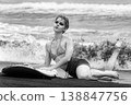 Stylish woman with short hair and surfboard posing on black sand beach. Black and white 138847756