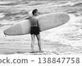 Woman with short hair holding surfboard stands in ocean. Black and white 138847758