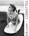Fashionable woman with short hair and makeup on surfboard at black sand beach 138847762