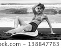 Moody black and white portrait of young woman with surfboard on black sand beach 138847763
