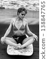 Monochrome portrait of pensive woman covered in sand sitting on surfboard 138847765