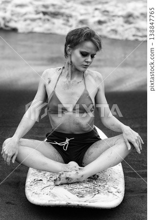 Monochrome portrait of pensive woman covered in sand sitting on surfboard 138847765