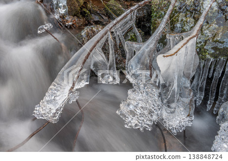 Frozen branches at edge of flowing stream during winter in forest Frozen branches at edge of flowing stream during winter in forest 138848724