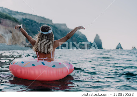 Woman, ocean, donut. Young woman on a donut float enjoys ocean view, arms raised in freedom with copy space. Woman, ocean, donut. Young woman on a donut float enjoys ocean view, arms raised in freedom with copy space. 138850528