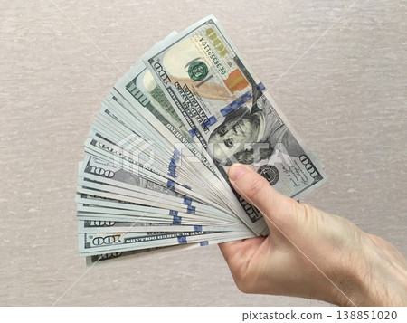 Hand holding a stack of hundred dollar bills against a simple background Hand holding a stack of hundred dollar bills against a simple background 138851020