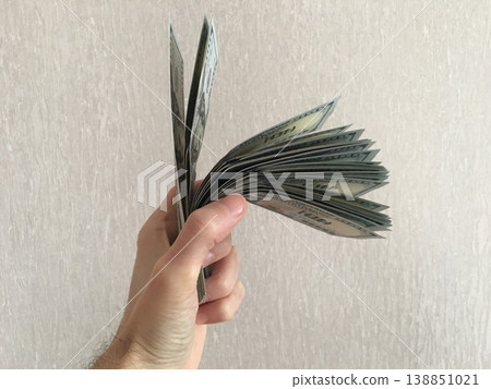 Hand holding fan of cash with more bills sticking out in front of plain background during daytime 138851021