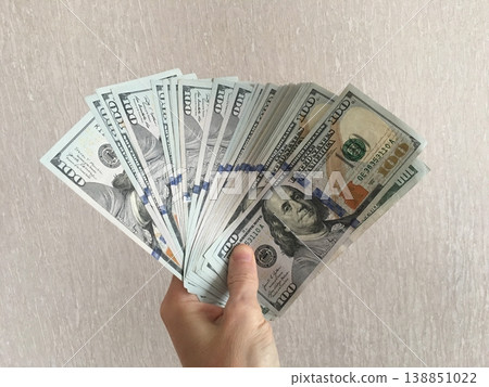 Person holds a fan of hundred dollar bills in front of a plain background during the daytime Person holds a fan of hundred dollar bills in front of a plain background during the daytime 138851022