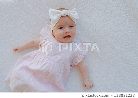 Baby girl lying on soft surface and moving naturally. Candid lifestyle shot showing early development and childhood activity. 138851228