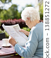A woman reading a newspaper in an open outdoor space. 138851272