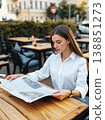 A woman reading a newspaper in an open outdoor space. 138851273
