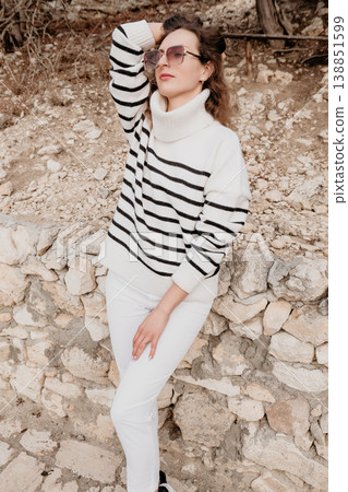 Woman fashion sweater poses against a rustic stone wall wearing a striped turtleneck and chic sunglasses in daylight 138851599