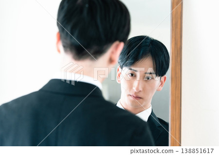 一名身穿西裝的男子在鏡子前整理儀容。 138851617