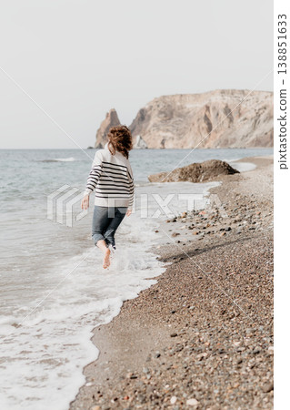 Seashore running woman runs barefoot on pebble beach towards sea with cliffs in background conveying freedom and copy space Seashore running woman runs barefoot on pebble beach towards sea with cliffs in background conveying freedom and copy space 138851633