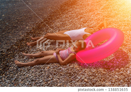 Woman girl beach lying on a pebble shore with a bright pink inflatable ring during a sunny summer vacation Woman girl beach lying on a pebble shore with a bright pink inflatable ring during a sunny summer vacation 138851635