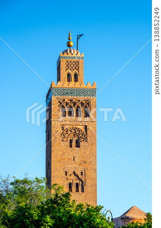 The tower of Kutubiyya Mosque stands tall in Marrakesh, Morocco. The clear blue sky forms a backdrop as the sun shines on this historical site. Visitors may be nearby, enjoying the scene. The tower of Kutubiyya Mosque stands tall in Marrakesh, Morocco. The clear blue sky forms a backdrop as the sun shines on this historical site. Visitors may be nearby, enjoying the scene. 138852249