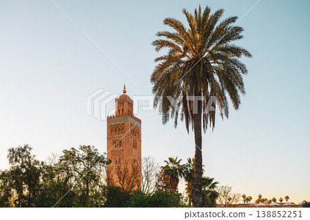 Kutubiyya Mosque is located in Marrakesh, Morocco, surrounded by palm trees. Visitors admire the scene as the sun begins to set in the sky, creating a lively atmosphere. Kutubiyya Mosque is located in Marrakesh, Morocco, surrounded by palm trees. Visitors admire the scene as the sun begins to set in the sky, creating a lively atmosphere. 138852251