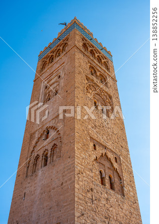 People gather around Kutubiyya Mosque in Marrakesh, Morocco. The sun shines brightly on the tall minaret. Visitors admire the historical architecture and take pictures. People gather around Kutubiyya Mosque in Marrakesh, Morocco. The sun shines brightly on the tall minaret. Visitors admire the historical architecture and take pictures. 138852256