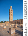 The Kutubiyya Mosque stands tall in Marrakesh, Morocco. People gather around as they admire the structure and the surrounding area during sunny weather. 138852258