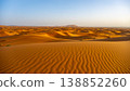 In the Sahara Desert, the vast sand dunes of Erg Chebbi stretch under a clear blue sky. The sun shines on the golden sands, highlighting the natural patterns formed by the wind. 138852260