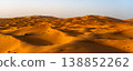 Visitors explore the vast sand dunes of Erg Chebbi in Merzouga, Sahara Desert, Morocco. The sun sets, casting golden light across the undulating landscape of fine sand. 138852262