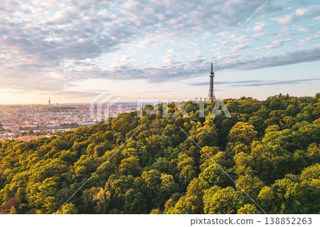 A stunning sunrise lights up the sky over the Petrin Lookout Tower in Prague. Nestled on a hill, the tower overlooks lush greenery and the city skyline, creating a serene atmosphere. 138852263