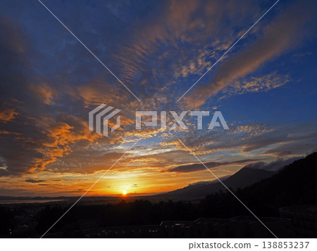 The sunset sinking between Mount Bandai and Lake Inawashiro. The orange sun and clouds against the blue sky are strikingly beautiful. The sunset sinking between Mount Bandai and Lake Inawashiro. The orange sun and clouds against the blue sky are strikingly beautiful. 138853237