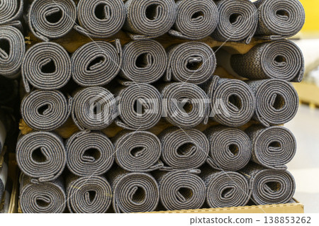 Industrial carpet production and storage with large rolls of textile flooring. Manufacturing process of various synthetic carpets in a warehouse or factory facility. Industrial carpet production and storage with large rolls of textile flooring. Manufacturing process of various synthetic carpets in a warehouse or factory facility. 138853262