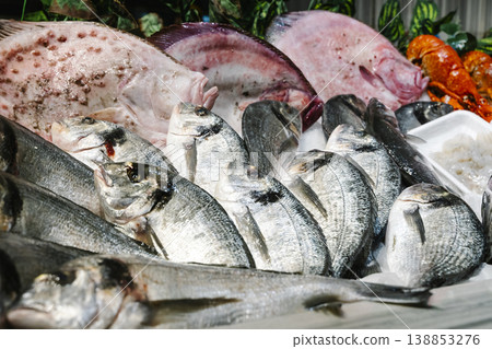 Fresh seafood assortment on ice at a traditional fish market. A variety of raw dorado, sea bream, and large fish fillets displayed with lobster for gourmet cooking Fresh seafood assortment on ice at a traditional fish market. A variety of raw dorado, sea bream, and large fish fillets displayed with lobster for gourmet cooking 138853276