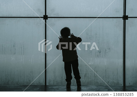 Silhouette of a lonely child looking through a large cold fogged window. A conceptual photography work exploring themes of childhood depression, psychological crisis, and the deep feeling of isolation 138853285