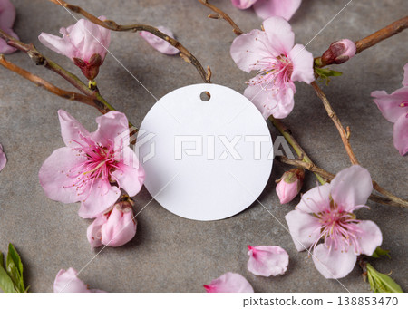 Blank round gift tag mockup with pink spring flowers and wooden twigs on grey stone, label design 138853470