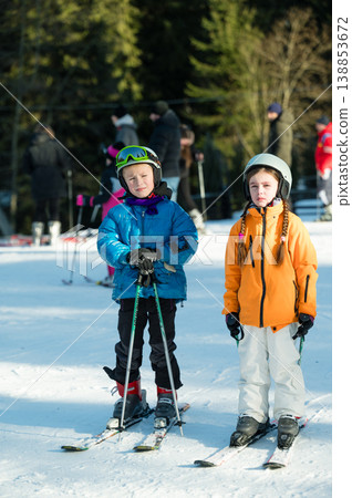 Young skiers enjoy a winter day on the slopes, dressed warmly and ready for adventure in a snowy mountain landscape surrounded by fellow ski enthusiasts Young skiers enjoy a winter day on the slopes, dressed warmly and ready for adventure in a snowy mountain landscape surrounded by fellow ski enthusiasts 138853672