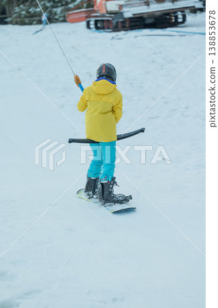 Young skier in bright yellow jacket navigates snowy slopes during winter afternoon, joyfully enjoying a fun day of winter sports activity with friends nearby 138853678