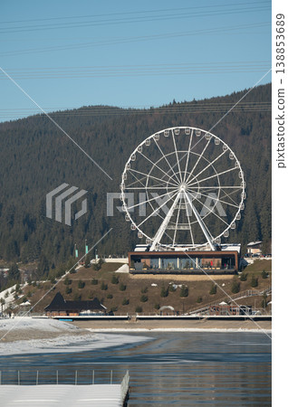 Majestic Ferris wheel stands tall against a serene winter landscape in the mountains, inviting visitors to enjoy breathtaking views at sunset 138853689