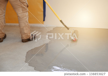 Worker applies concrete coating to a self-leveling floor using a roller in a construction site in the morning time Worker applies concrete coating to a self-leveling floor using a roller in a construction site in the morning time 138853827