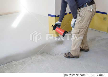 Worker applies sealant to concrete floor in modern indoor space during construction process. Priming and moistening the base for self-leveling floors. Worker applies sealant to concrete floor in modern indoor space during construction process. Priming and moistening the base for self-leveling floors. 138853868