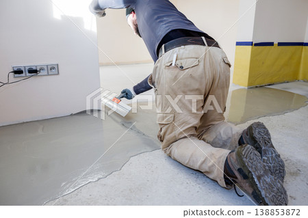 Construction worker applying cement on floor in empty room during renovation project near electrical outlets Construction worker applying cement on floor in empty room during renovation project near electrical outlets 138853872