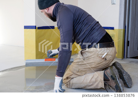 Worker smooths wet concrete in a room during a construction project in a residential area 138853876